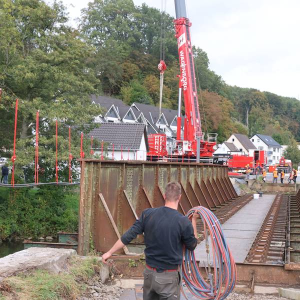 Ein Mann trägt Kabel. Im Hintergrund ist ein Kran an der Aggerbrücke erkennbar.