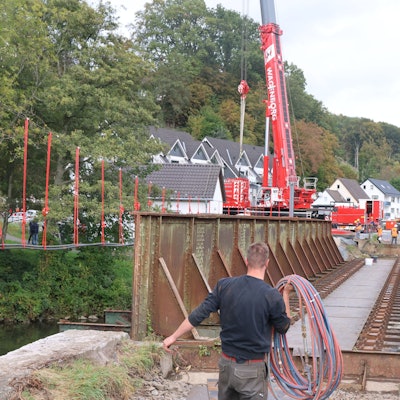 Ein Mann trägt Kabel. Im Hintergrund ist ein Kran an der Aggerbrücke erkennbar.