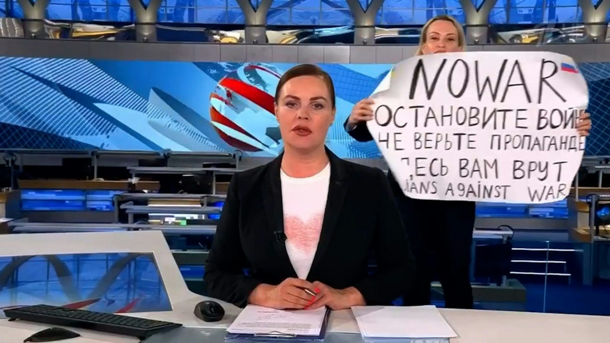 Mitte März 2022 zeigt die russische Journalistin in der abendlichen Hauptnachrichtensendung des russischen Staatsfernsehens ihr Plakat. Damit protestierte sie im Live-TV gegen die Invasion in der Ukraine.