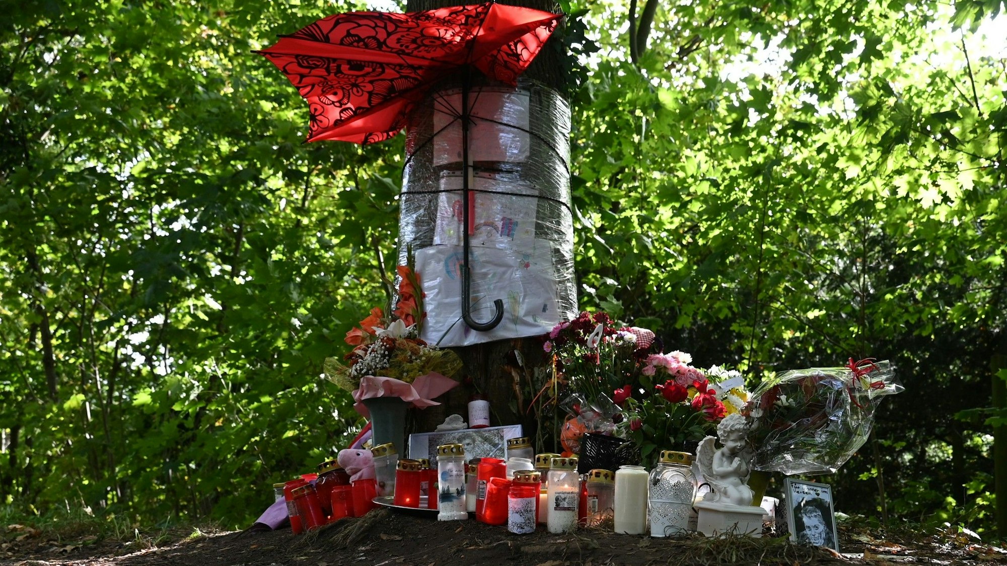 Das Bild zeigt einen Baum, vor dem Blumen, Kerzen und Bilder niedergelegt wurden.
