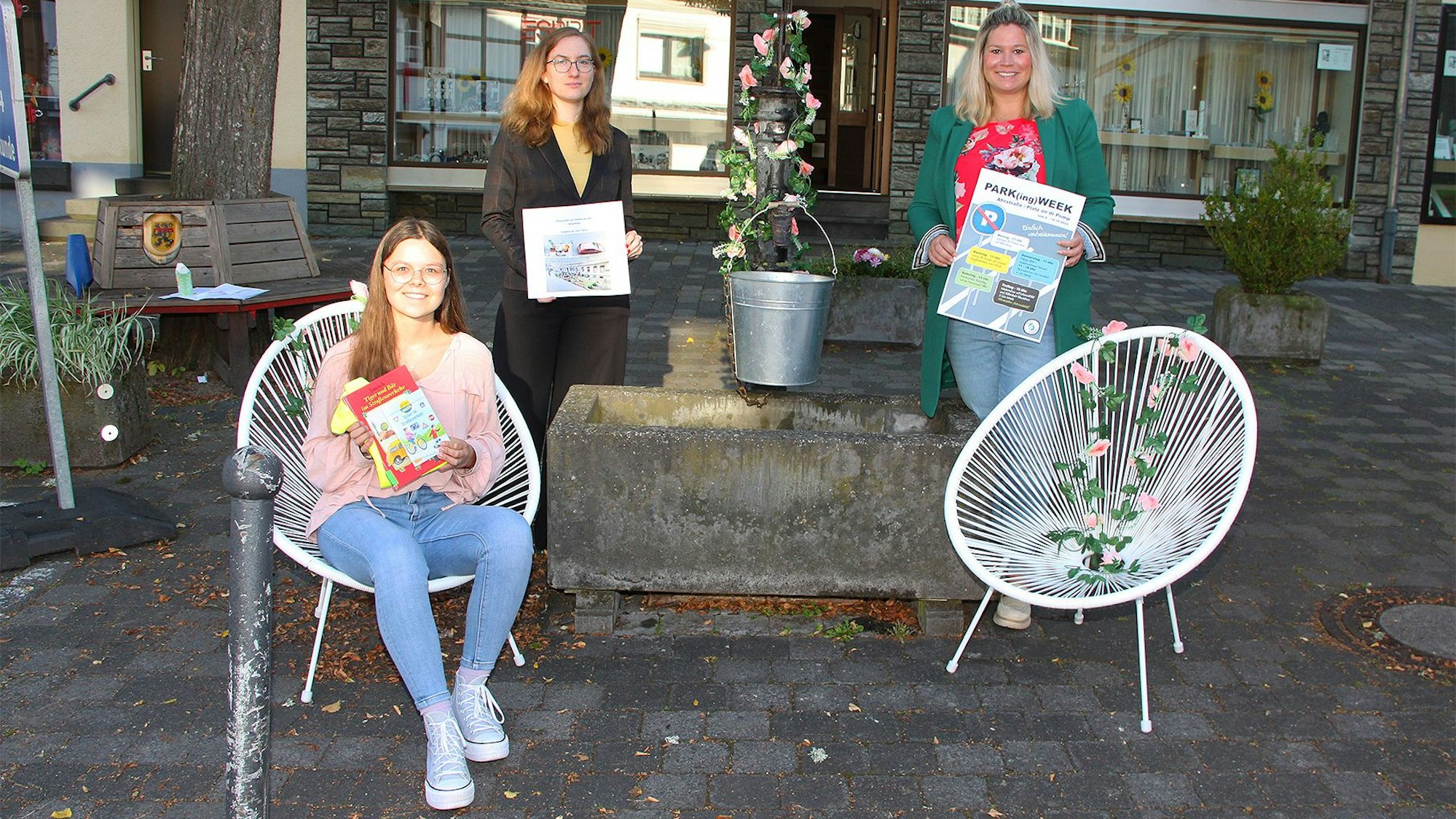 An einer alten Brunnenpumpe werben drei Frauen, Bürgermeisterin Jennifer Meuren (v.r.), Michelle Karschat und Viktoria Thur für die Kunstaktion.