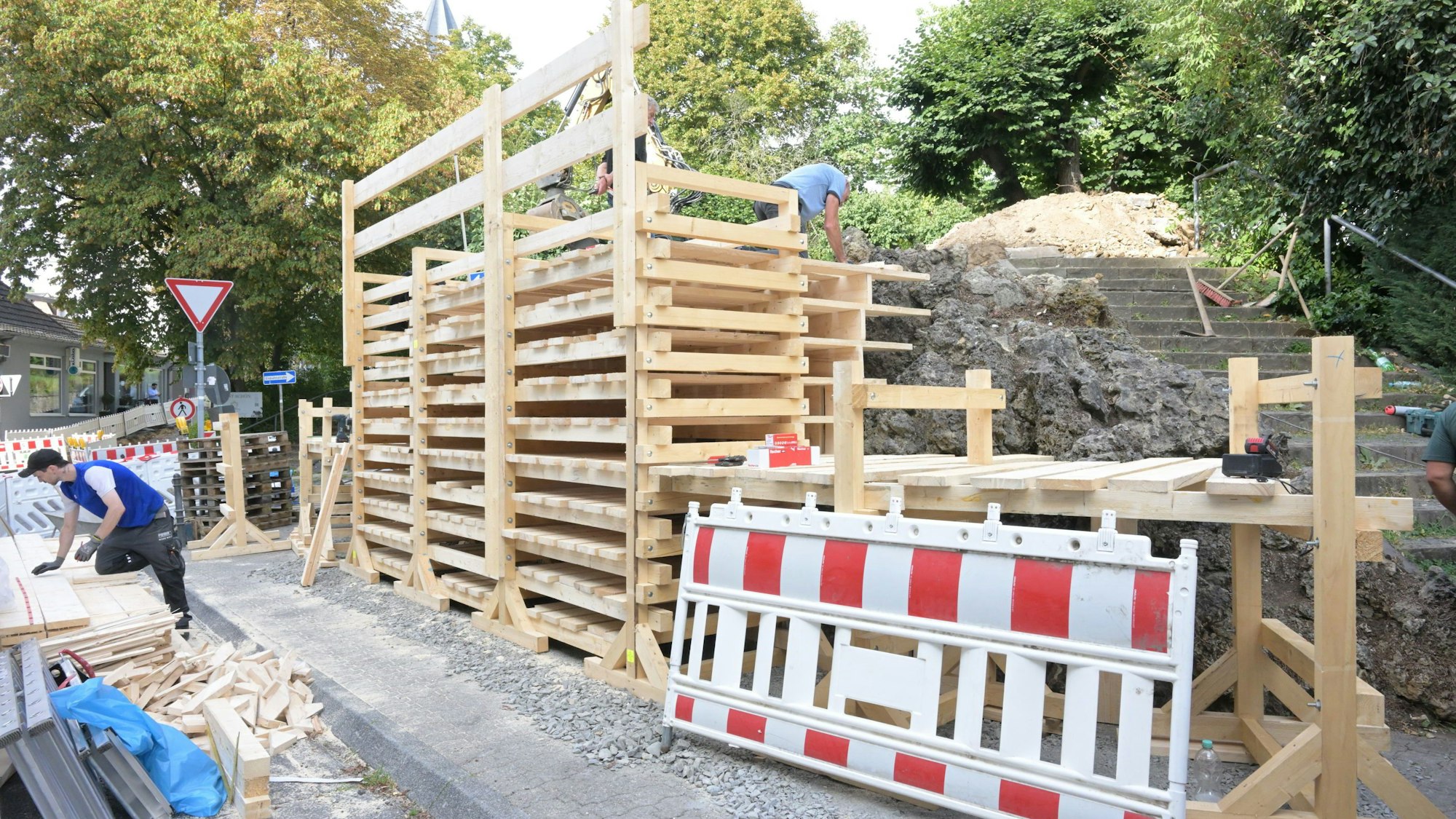 Ein Gerüst aus übereinander montierten Holzbrettern ist vor dem Brunnen montiert.