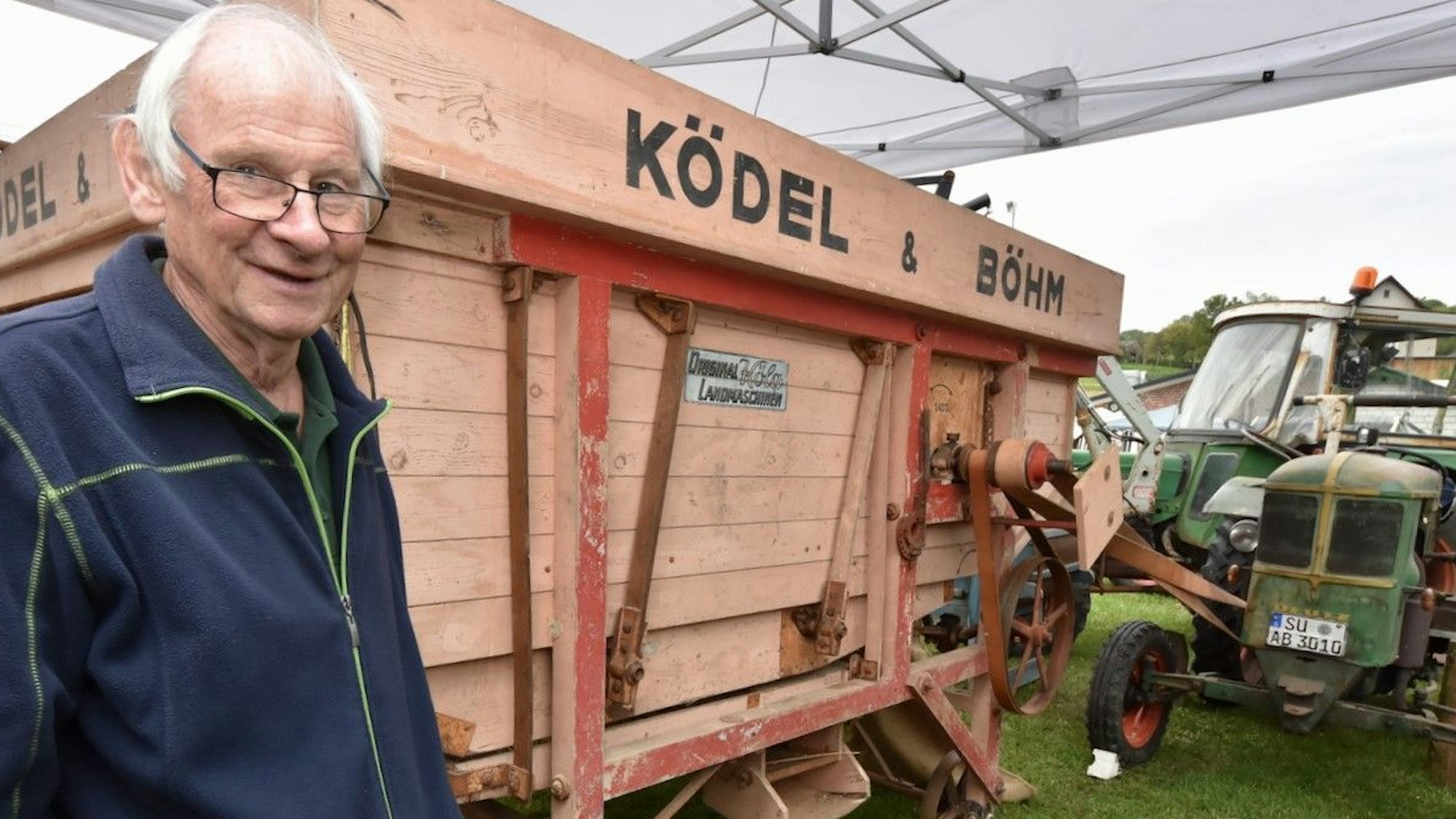 Der Mitgründer der Deutz-Schlepper-Freunde, Manfred Keuenhof, steht neben einer sehr alten Dreschmaschine und einem Traktor-Oldtimer.