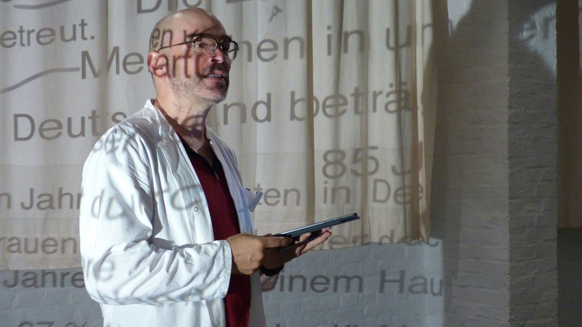 Ein Mitglied des Ensembles ist als Wissenschaftler verkleidet, er trägt eine Brille und einen weißen Kittel.