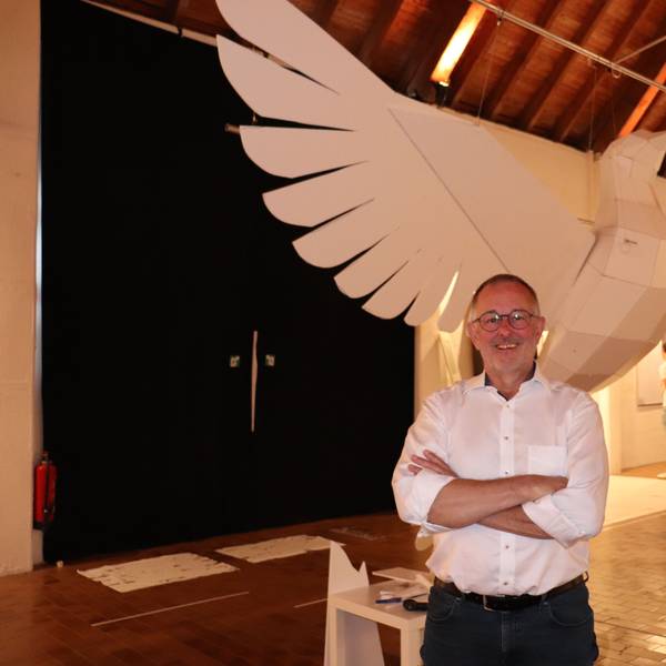 Eine riesige Taube aus Kunststoff hängt in einem Ausstellungsraum, davor steht der Künstler Manni Vogel, der sie gebaut hat.