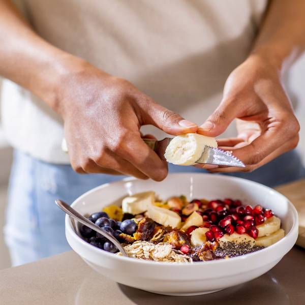 Jemand schneidet Bananenstücke in eine Müsli-Schale.
