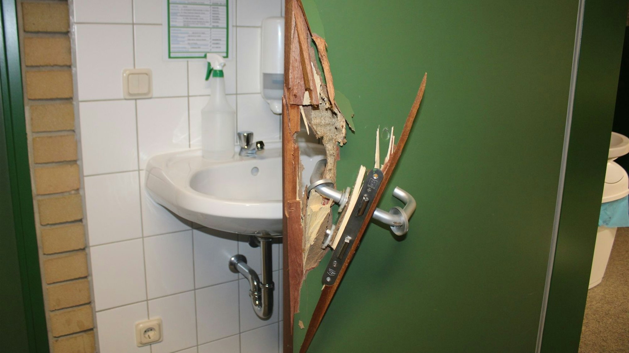 Eine grüne Tür wurde aufgebrochen, Klinke und Schloss sind herausgebrochen, ein Loch klafft im Holz.