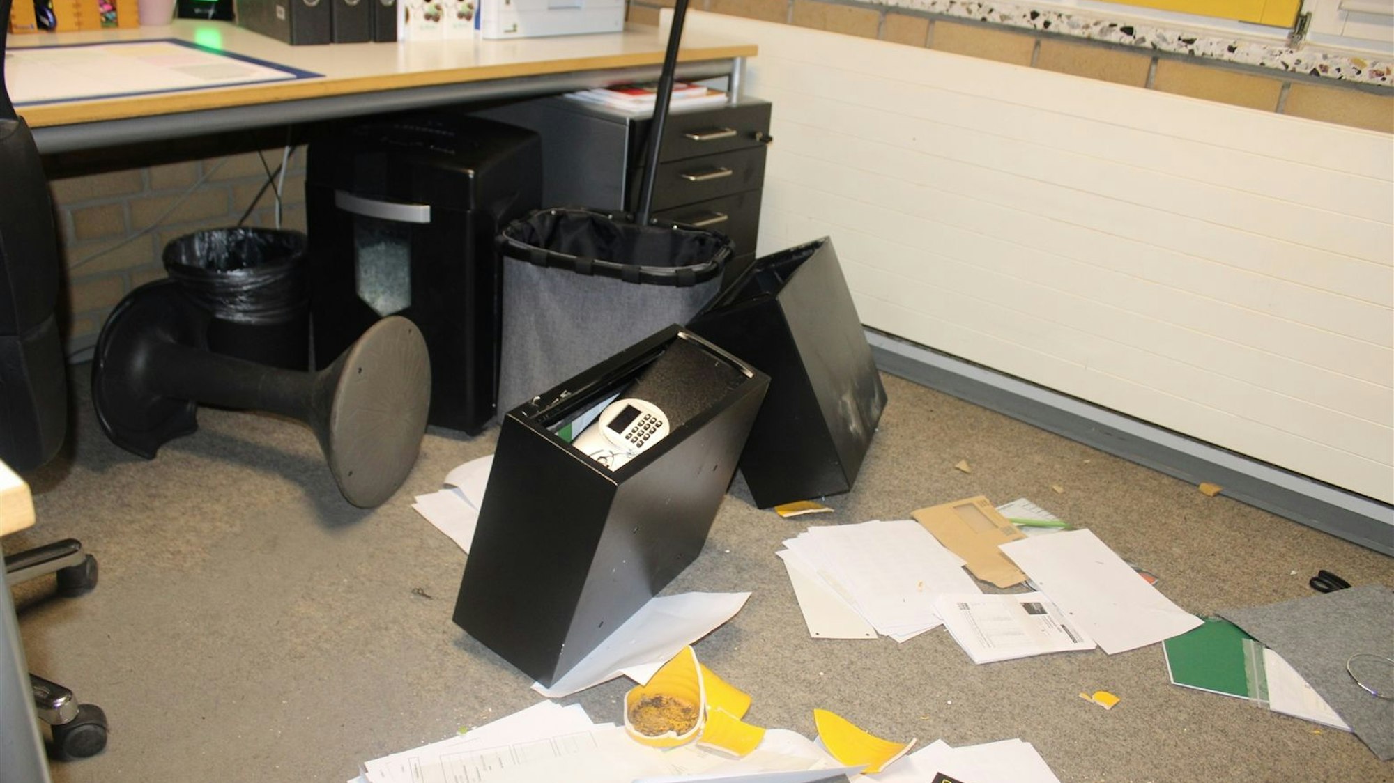 Auf dem Boden eines Büros liegt ein aufgebrochener Tresor, Papiere und zerschlagene Gegenstände.