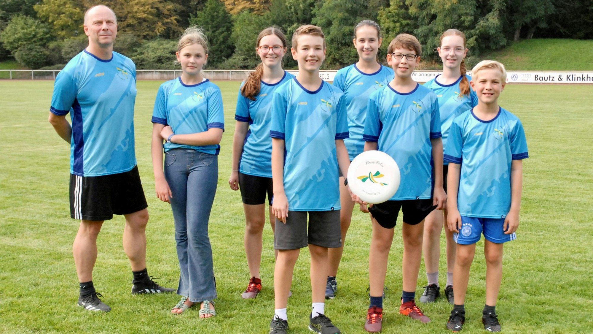 Ein Mann, Mädchen und Jungen stehen in blauen Trikots auf einem Rasenplatz.