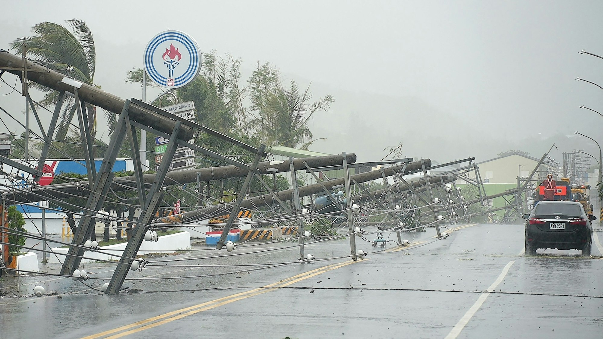 A car passes by power lines downed by the high winds from Typhoon Koinu in Taiwan's southern Pingtung County on October 5, 2023. Typhoon Koinu grazed the southern edge of Taiwan on October 5, blanketing the region in torrential rain and bringing record-breaking winds of more than 340 kilometres an hour to an outlying island. (Photo by Sean CHANG / AFP)
