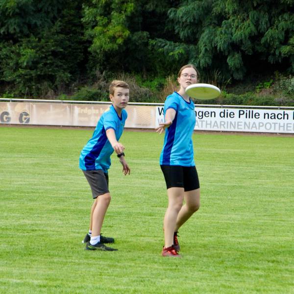 Ein Mädchen wirft eine Frisbee-Scheibe, ein Junge deckt sie.