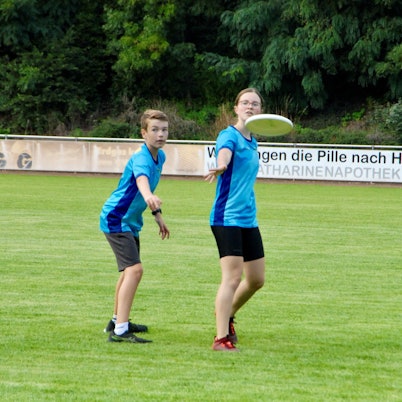 Ein Mädchen wirft eine Frisbee-Scheibe, ein Junge deckt sie.