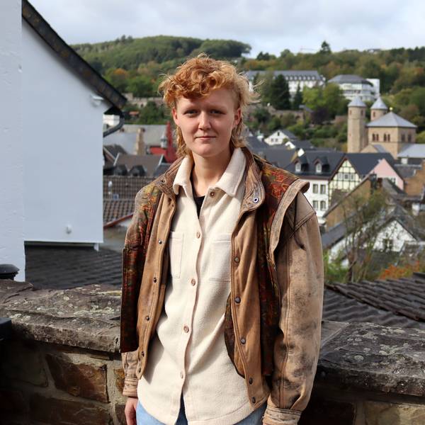 Die Schauspielerin und Musikerin Svea Kirschmeier lehnt an einer hüfthohnen Bruchsteinmauer. Hinter ihr die ist Kulisse Bad Münstereifels zu erkennen.