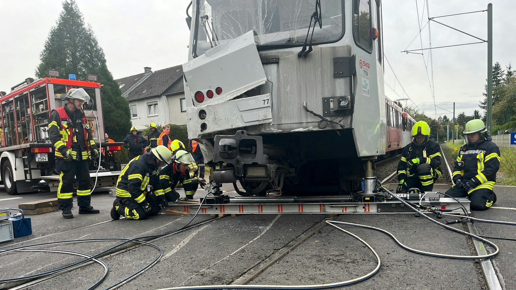 Arbeiter knien rechts und links von der beschädigten Straßenbahn und versuchen, sie mit Arbeitsgeräten anzuheben.