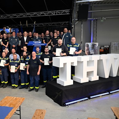THWler stehen mit Urkunden und Medaillen hinter einem großen weißen Schriftzug „THW“.