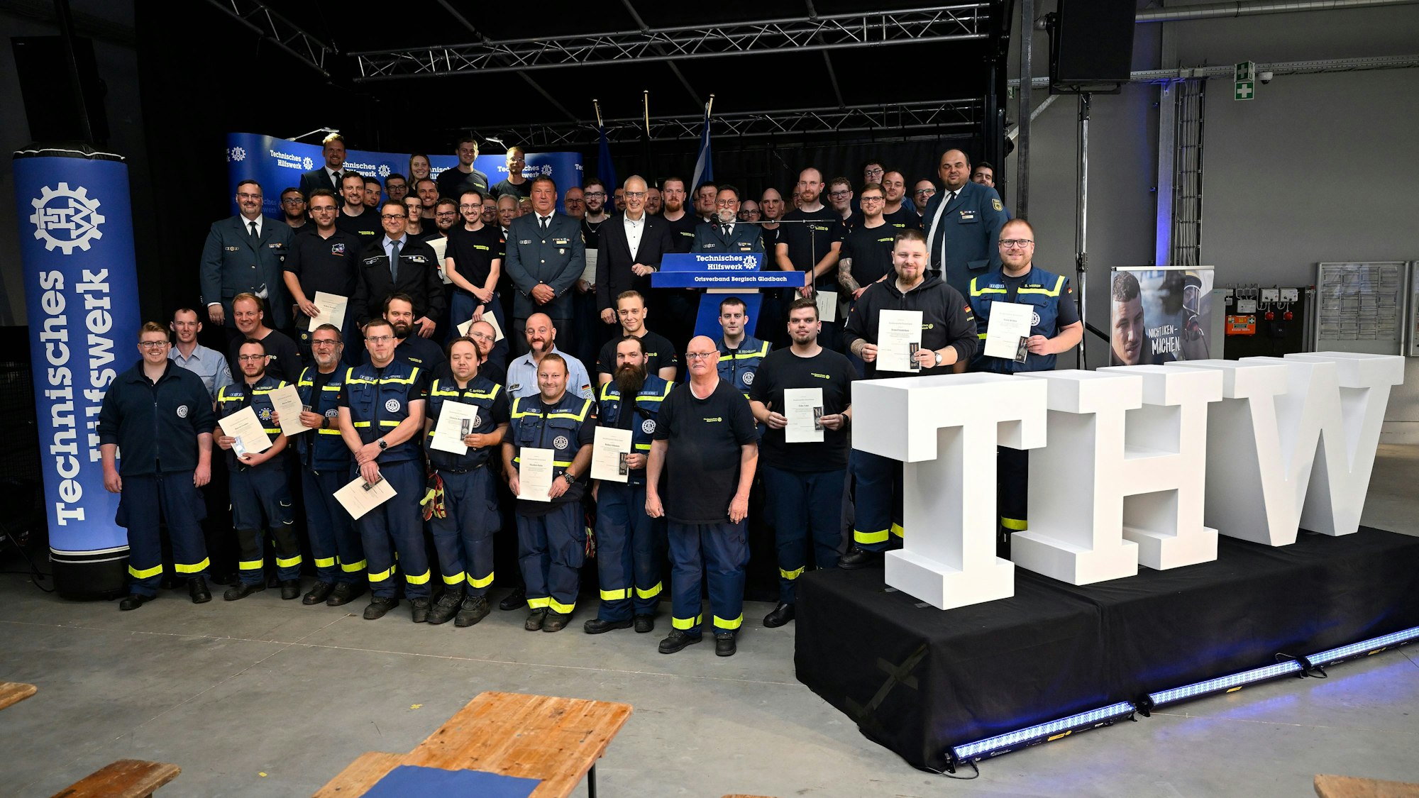THWler stehen mit Urkunden und Medaillen hinter einem großen weißen Schriftzug „THW“.