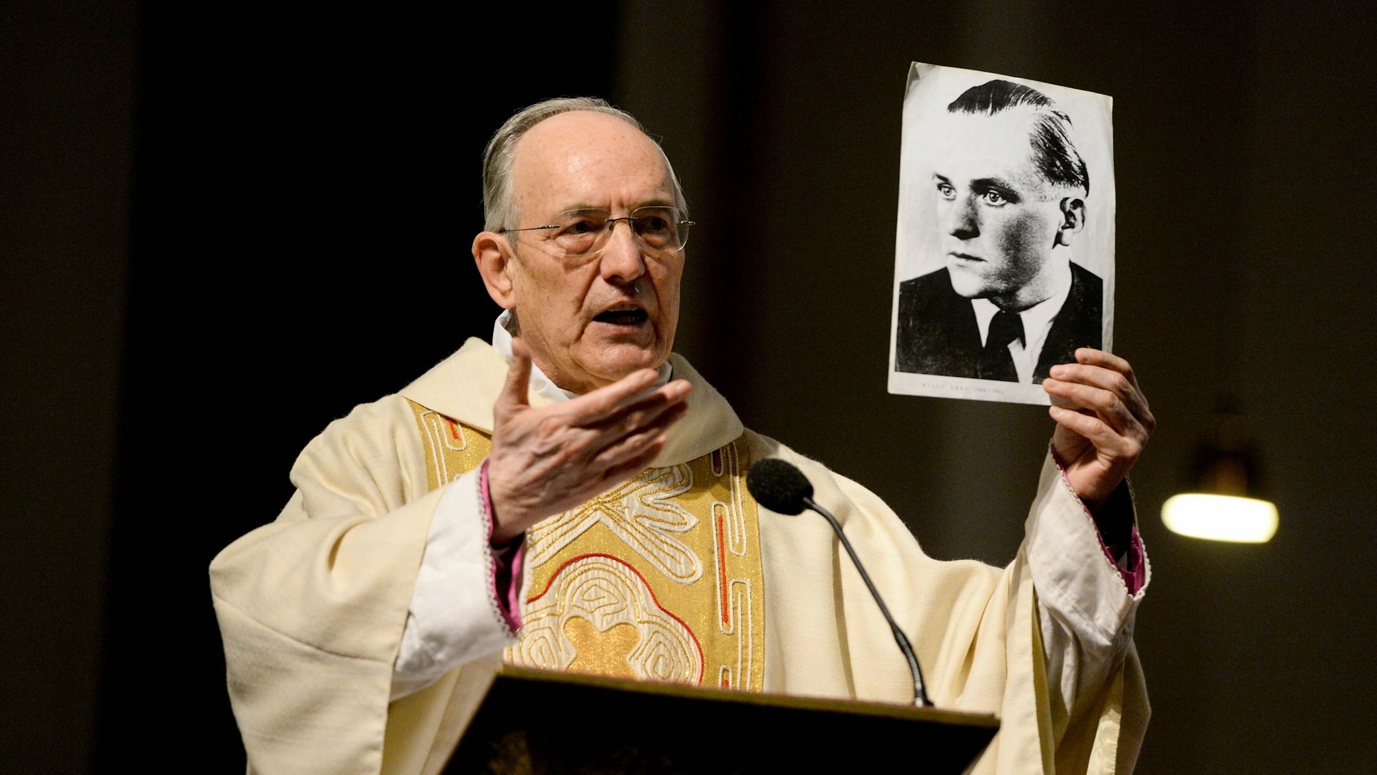 Prälat Prof. Dr. Helmut Moll 2013 im Priestergewand. Er hält ein Foto von Willi Graf in der Hand.