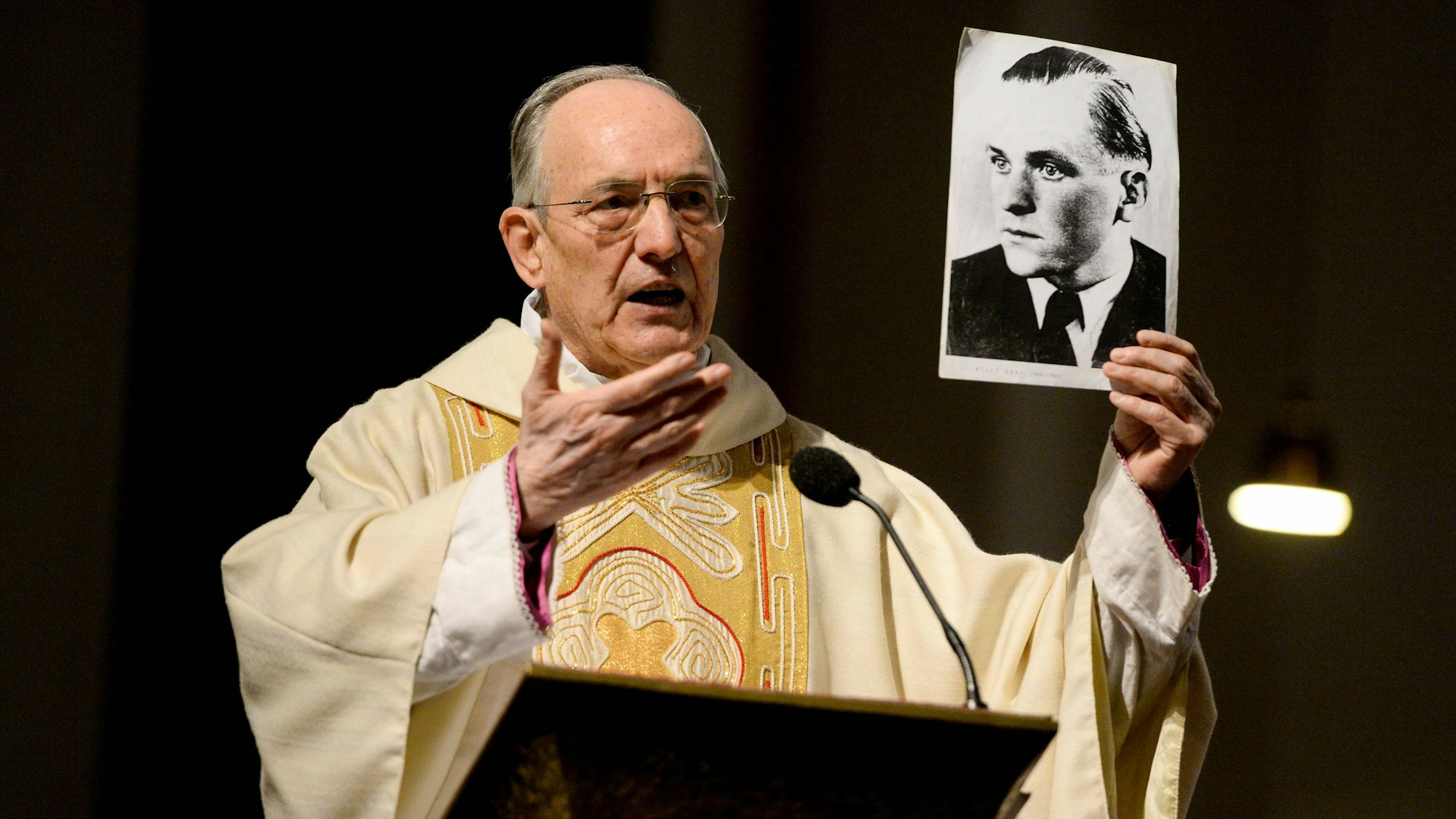 Der Geistliche Helmut Moll spricht in der Euskirchener Herz-Jesu-Kirche über Willi Graf und hält ein Foto in der Hand, das den Widerstandskämpfer zeigt.
