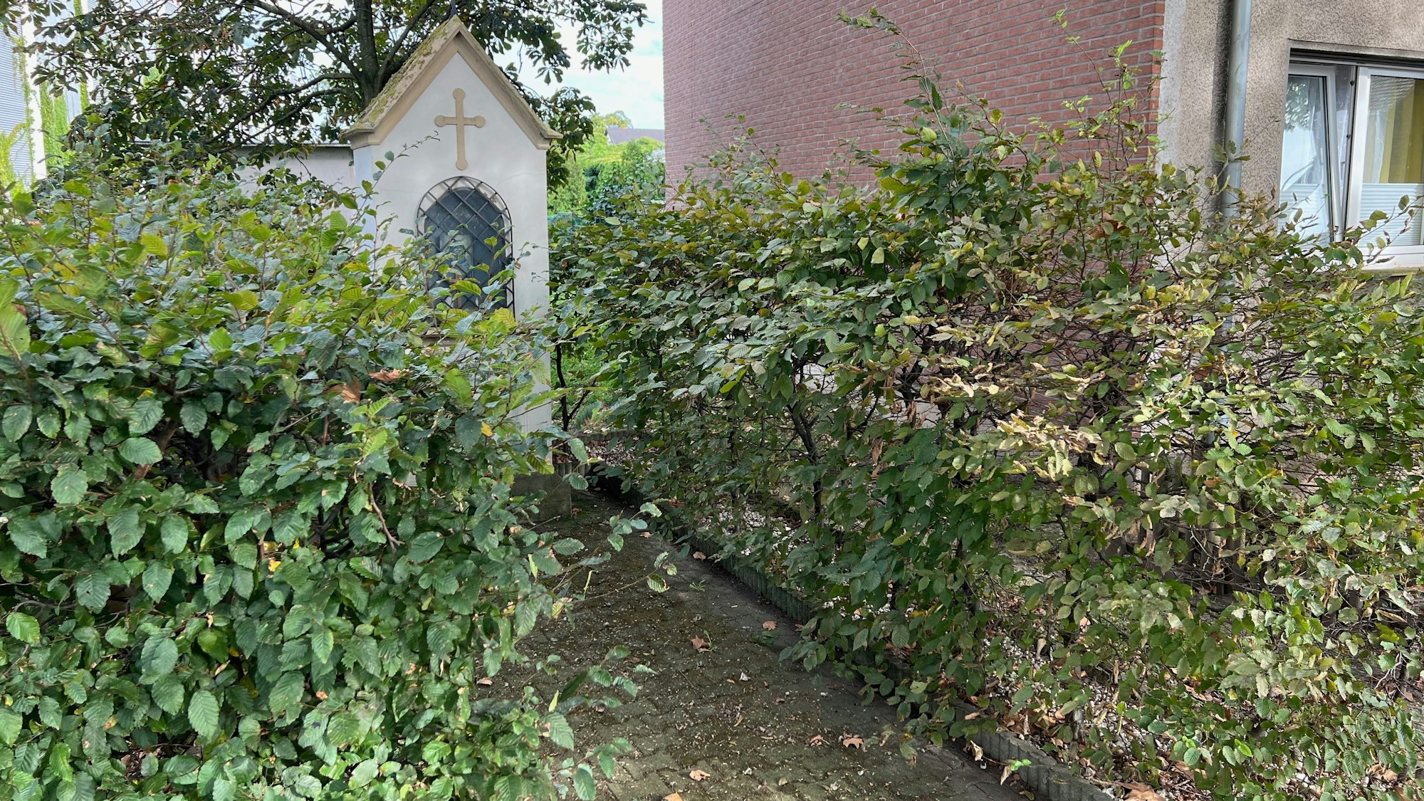 Das Bild zeigt ein Heiligen-Häuschen hinter einer Hecke.