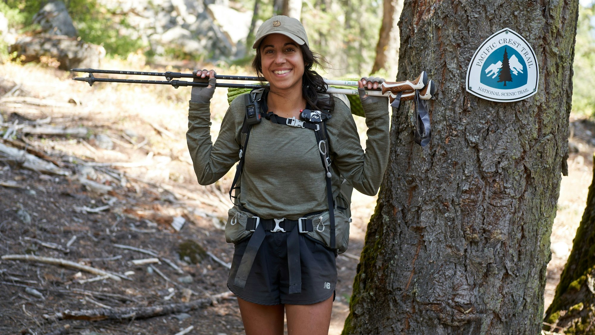 Miriam Wiesner hat die Trecking-Stöcke über die Schulter gelegt und schaut am Rande des PCT in die Kamera.