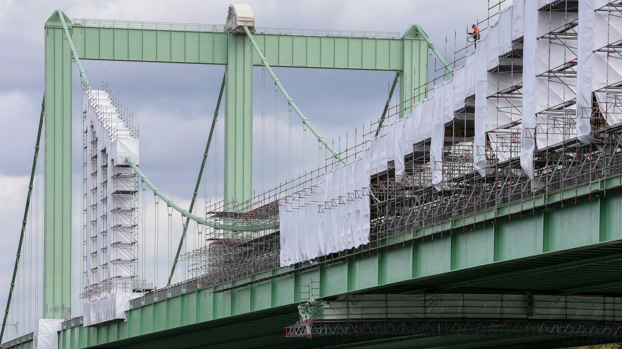 Teile der grünen Autobahnbrücke sind mit einem Baugerüst eingerüstet. Das Gerüst ist an vielen Stellen mit weißen Planen verhüllt.