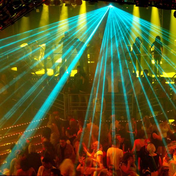 Eine Laseranlage beleuchtet eine tanzende Menschenmenge in einer Großraumdiscothek.