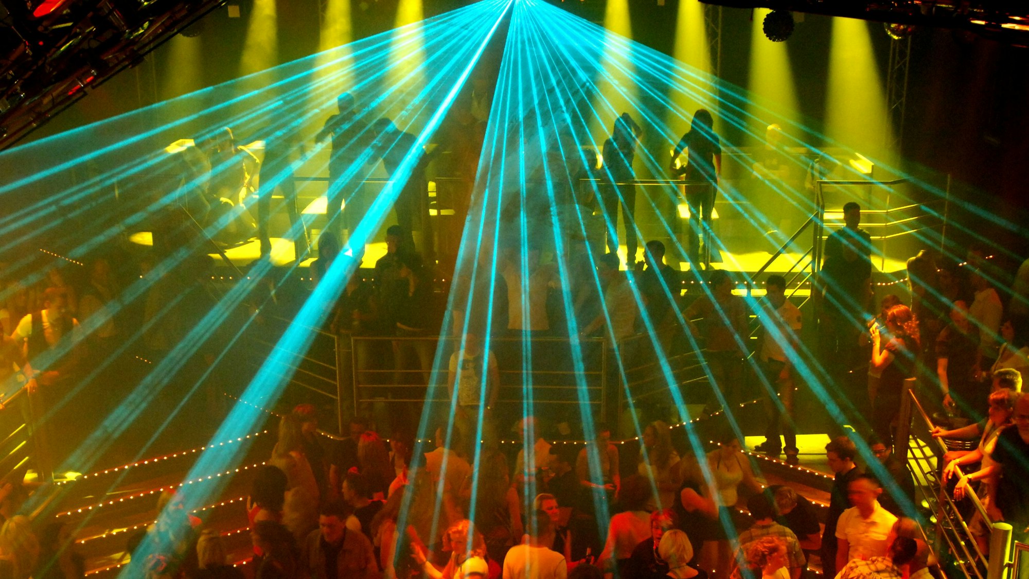 Eine Laseranlage beleuchtet eine tanzende Menschenmenge in einer Großraumdiscothek.