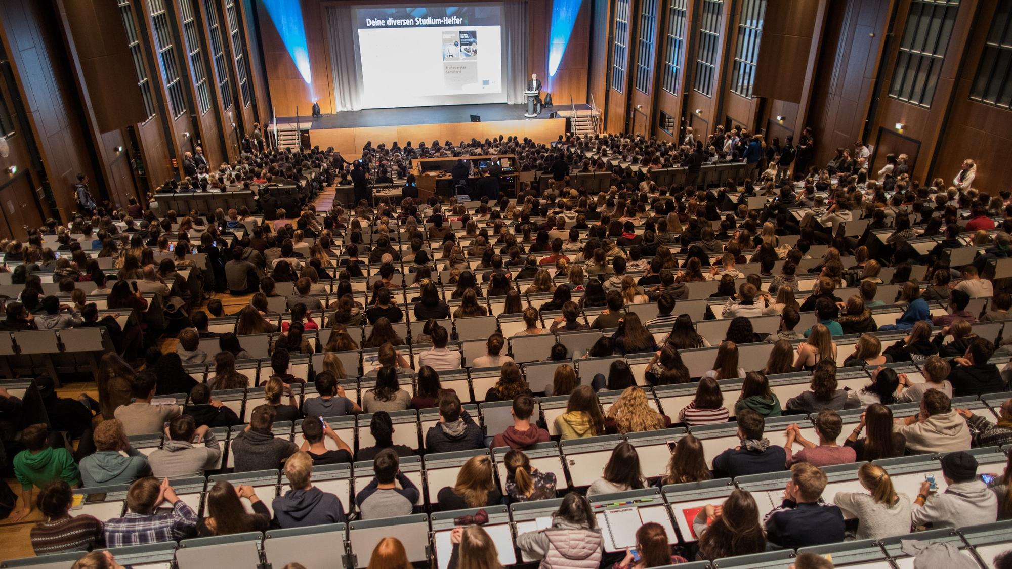 Studenten verfolgen im Hörsaal im Hauptgebäude der Universität zu Köln die Erstsemesterbegrüßung.
