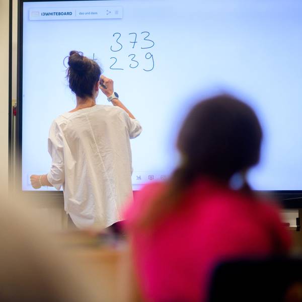 Eine Lehrerin schreibt eine Mathematikaufgabe auf eine digitale Schultafel im Klassenraum einer 4. Klasse einer Grundschule.