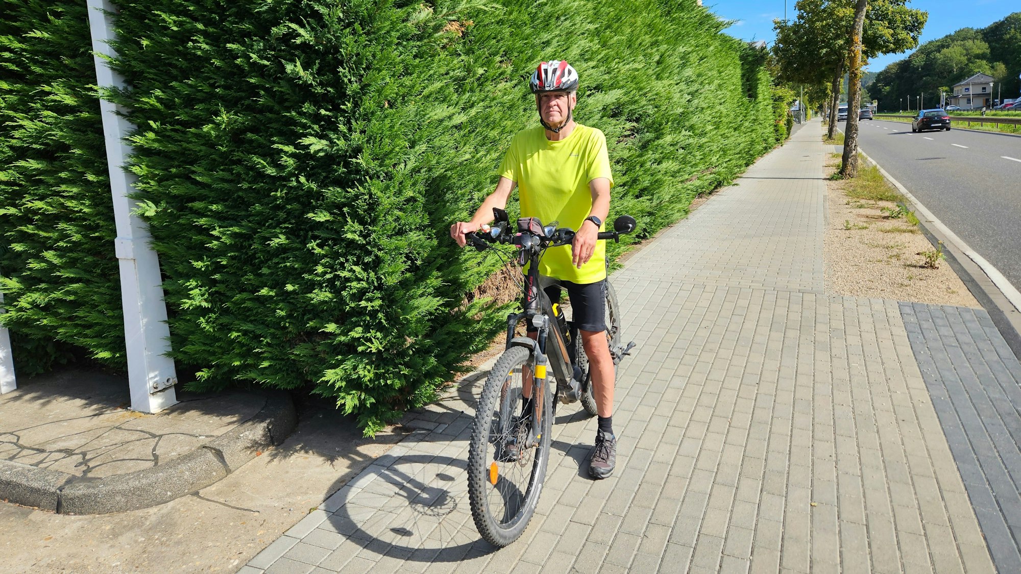 Wolfgang Röhrich ist mit seinem Fahrrad auf dem Radweg an der Bundesstraße in Gemünd unterwegs. Er hat an einer gefährlichen Einfahrt an einer Hecke angehalten.