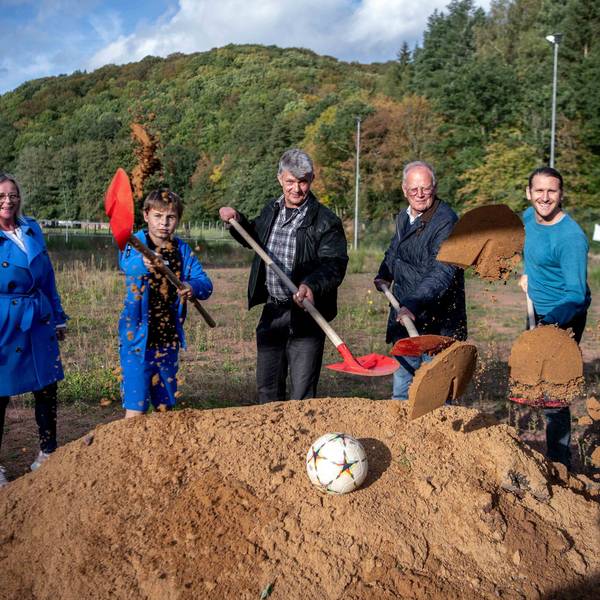 Das Bild zeigt den offiziellen Spatenstich. Die Beteiligten werfen Sand mithilfe von Schaufeln in Richtung Kamera.