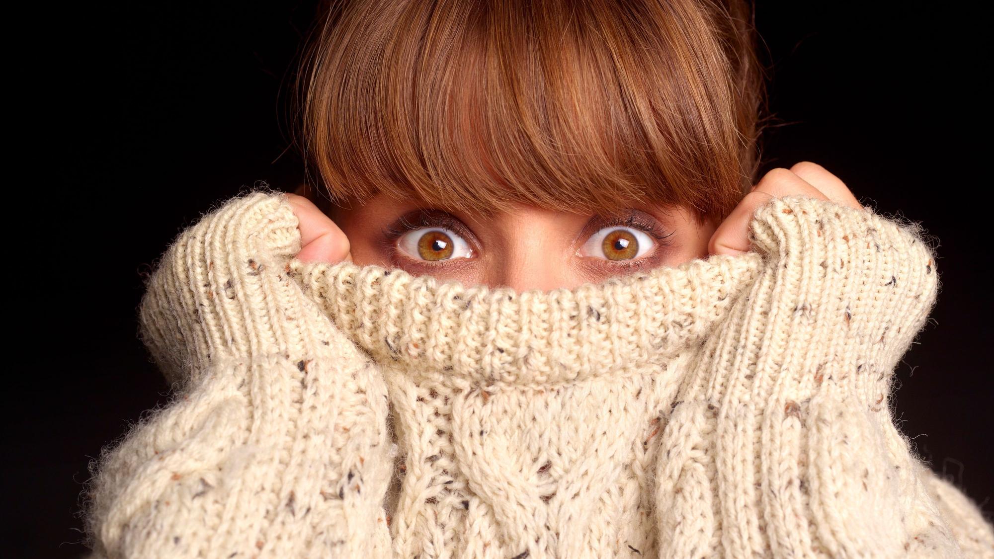 Junge Frau verkriecht sich in bis über die Nase in ihrem Pullover