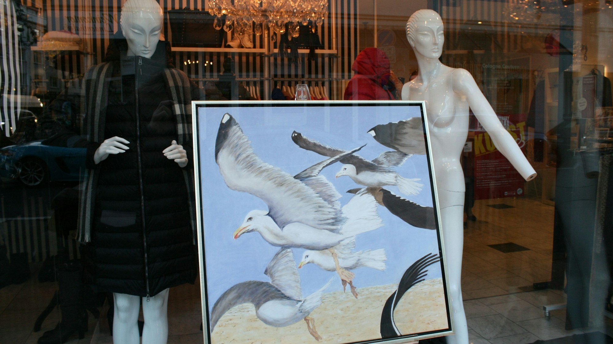 In einem Schaufenster ist zwischen zwei Schaufensterpuppen ein großformatiges Möwen-Gemälde zu sehen.
