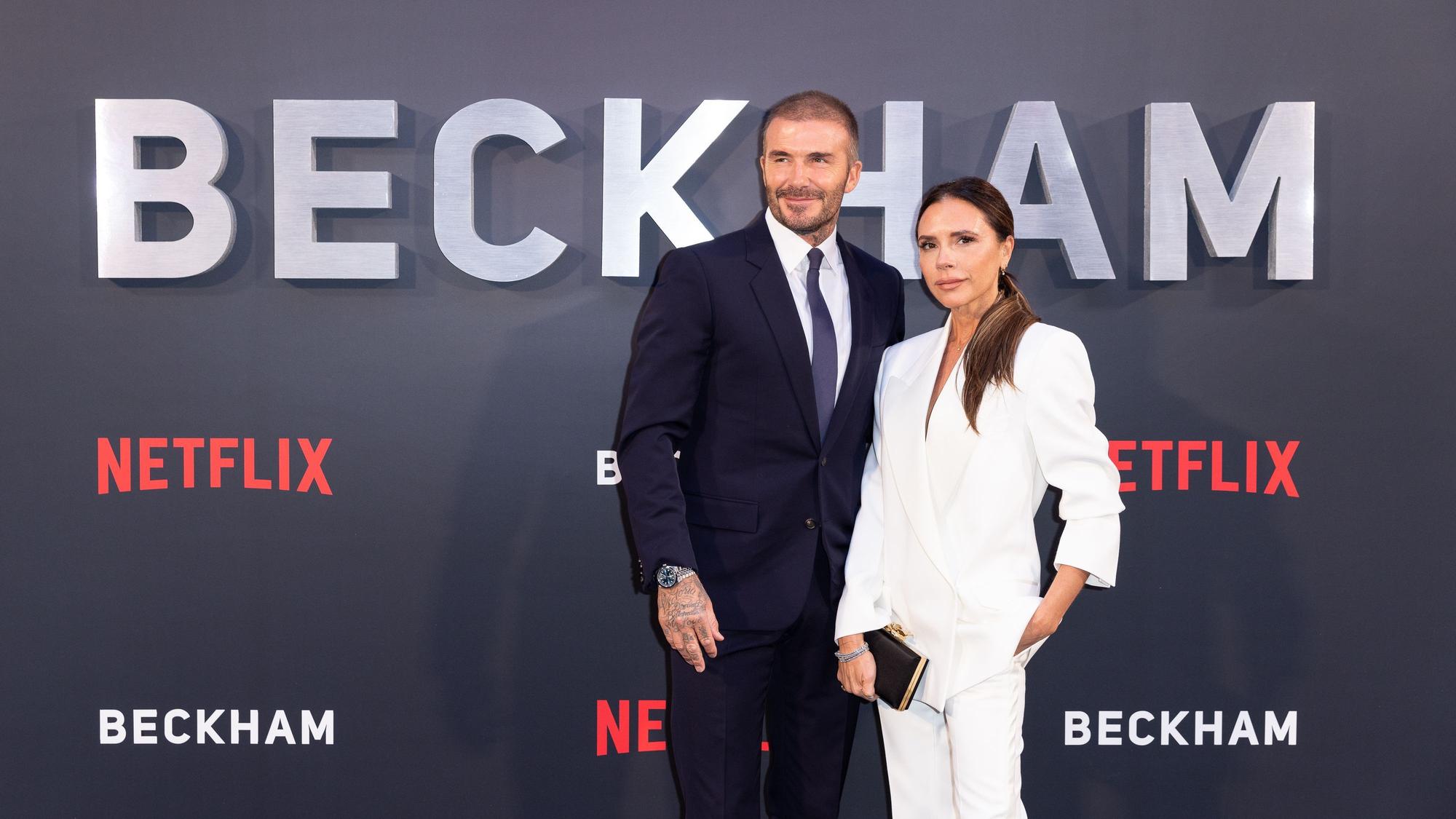 David Beckham und Victoria Beckham bei der Premiere der vierteiligen Miniserie in London. Er trägt einen schwarzen Anzug, sie einen weißen Hosenanzug.