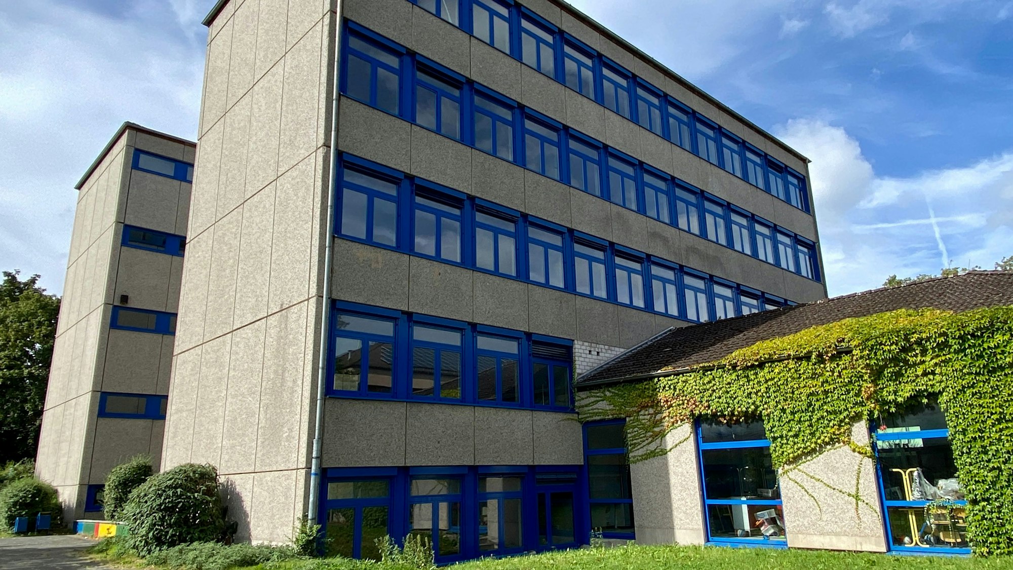 Das Gymnasium ist ein graues Schulgebäude mit blauen Fensterrahmen.