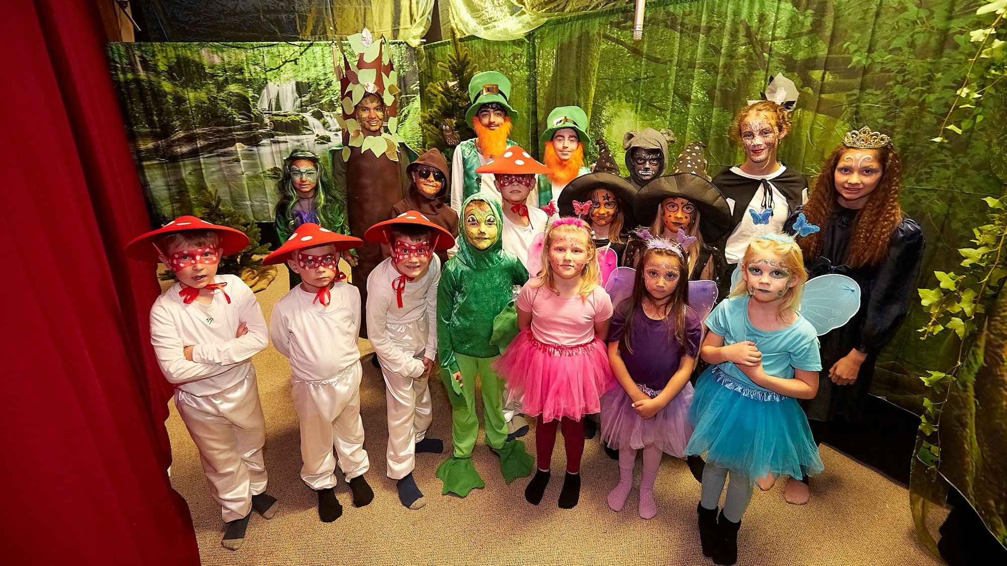 Die Kinder des Theatervereins Nettersheim stehen in ihren Kostümen auf der Theaterbühne, die eine Wald-Kulisse zeigt.