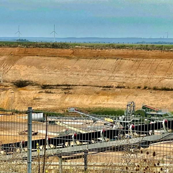 Blick in eine Kiesgrube mit Windrädern im Hintergrund.