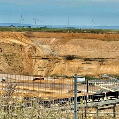 Blick in eine Kiesgrube mit Windrädern im Hintergrund.