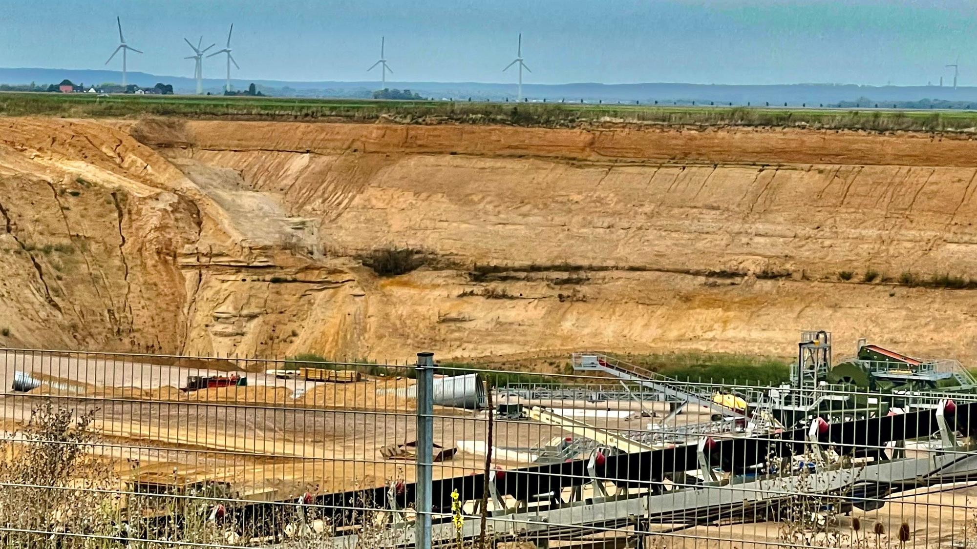 Blick in eine Kiesgrube mit Windrädern im Hintergrund.