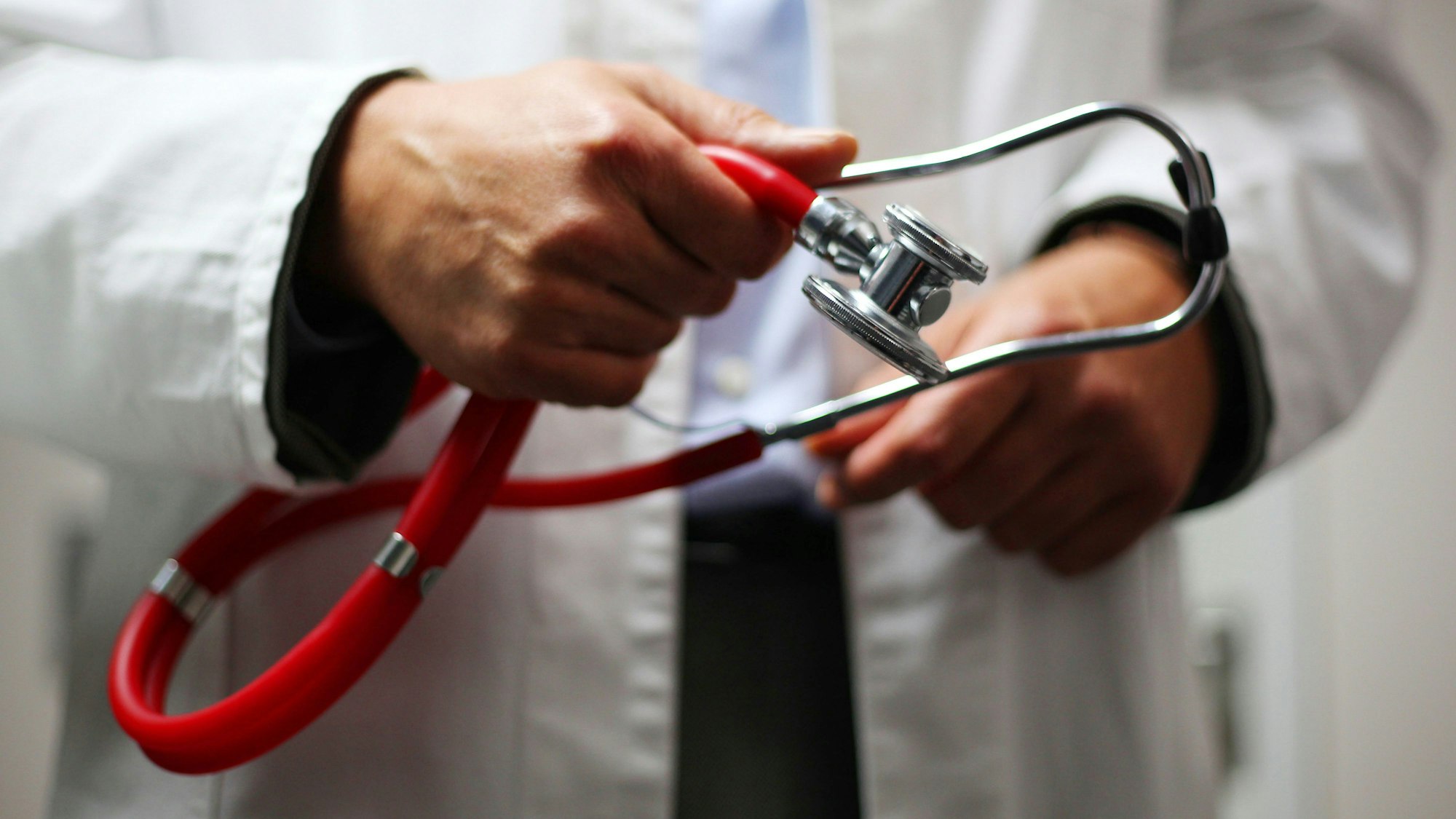 Ein Arzt in weißem Kittel hält ein Stethoskop in den Händen.
