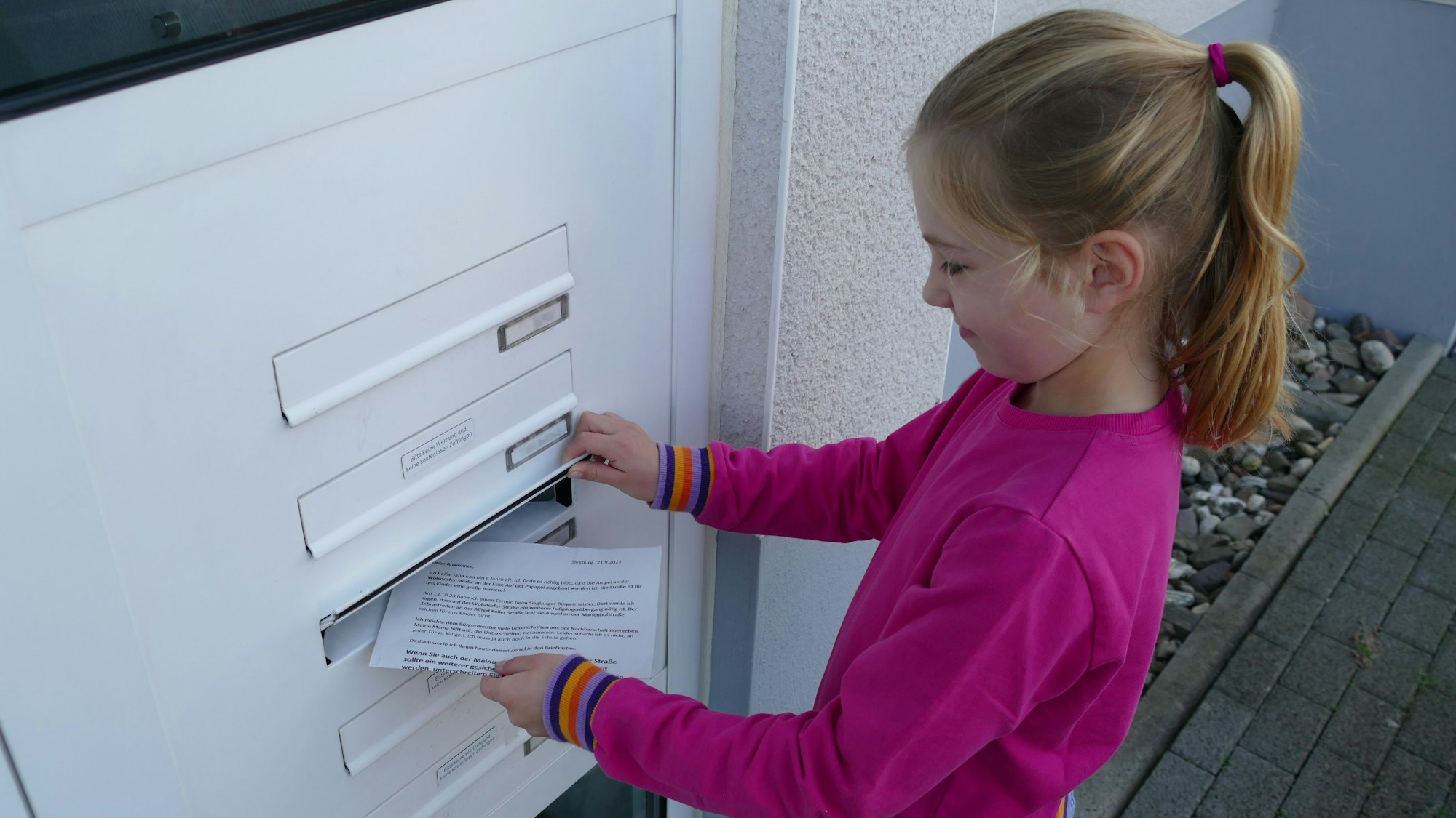 Ein Mädchen wirft einen Zettel in einen Briefkasten.
