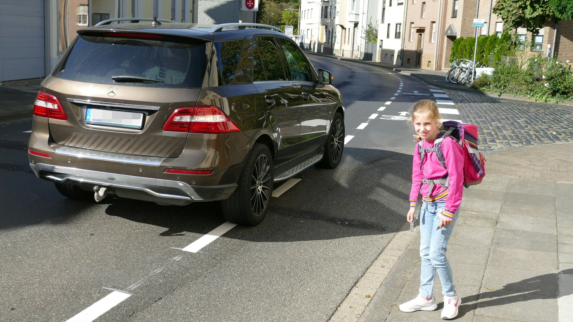 Ein Mädchen steht an einer Straße. Ein Auto fährt vorbei.