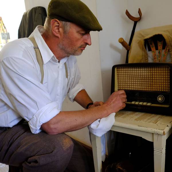 Peter Drespa verkörpert einen Kriegsheimkehrer des Zweiten Weltkriegs im Freilichtmuseum Kommern. In der Kleidung der späten 1940-er Jahre kniet er vor einem Radio, das auf einem Küchenstuhl steht.