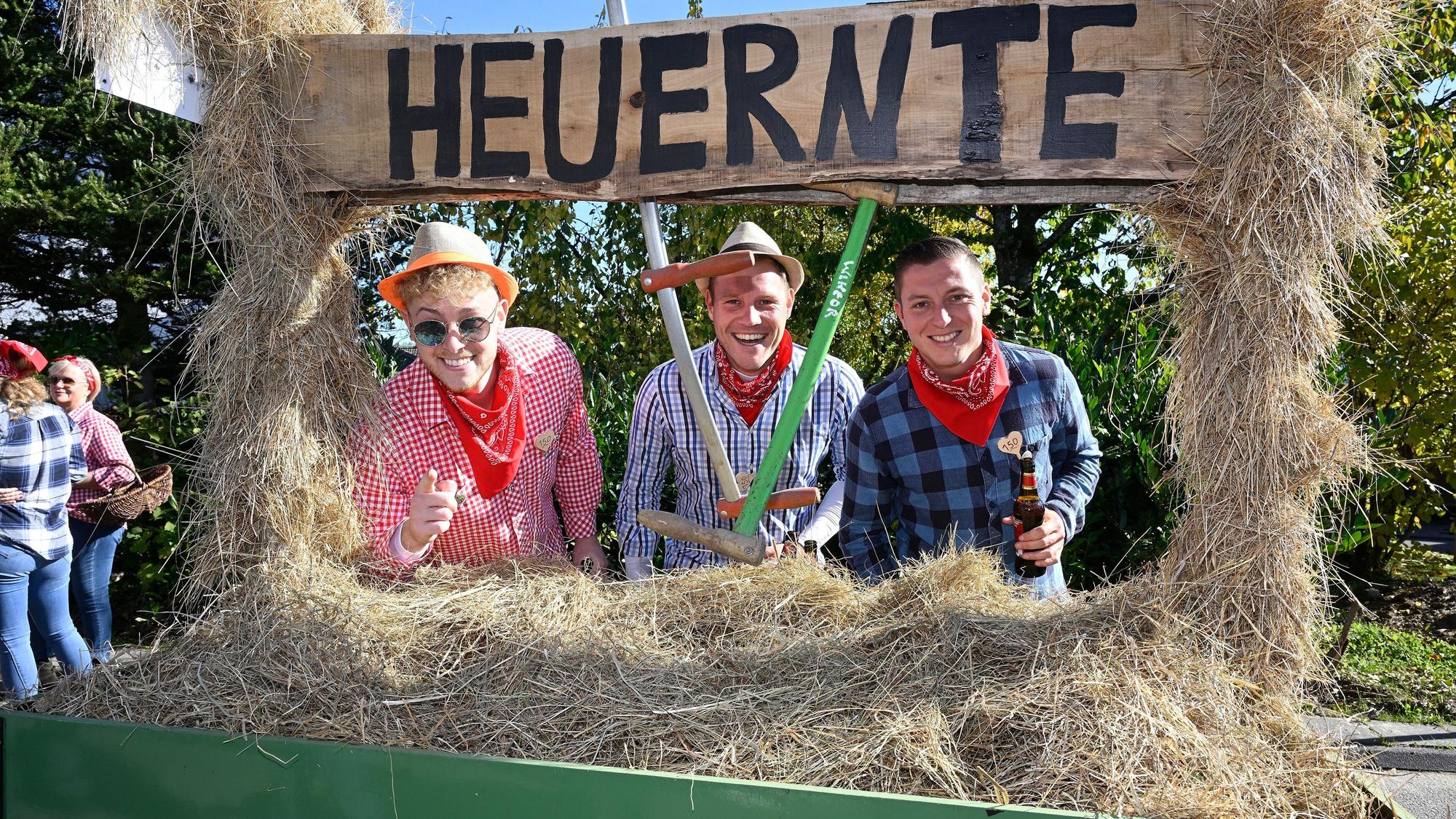 Drei Menschen stehen mit Arbeitsgerät hinter einem mit Heu beladenen Wagner.