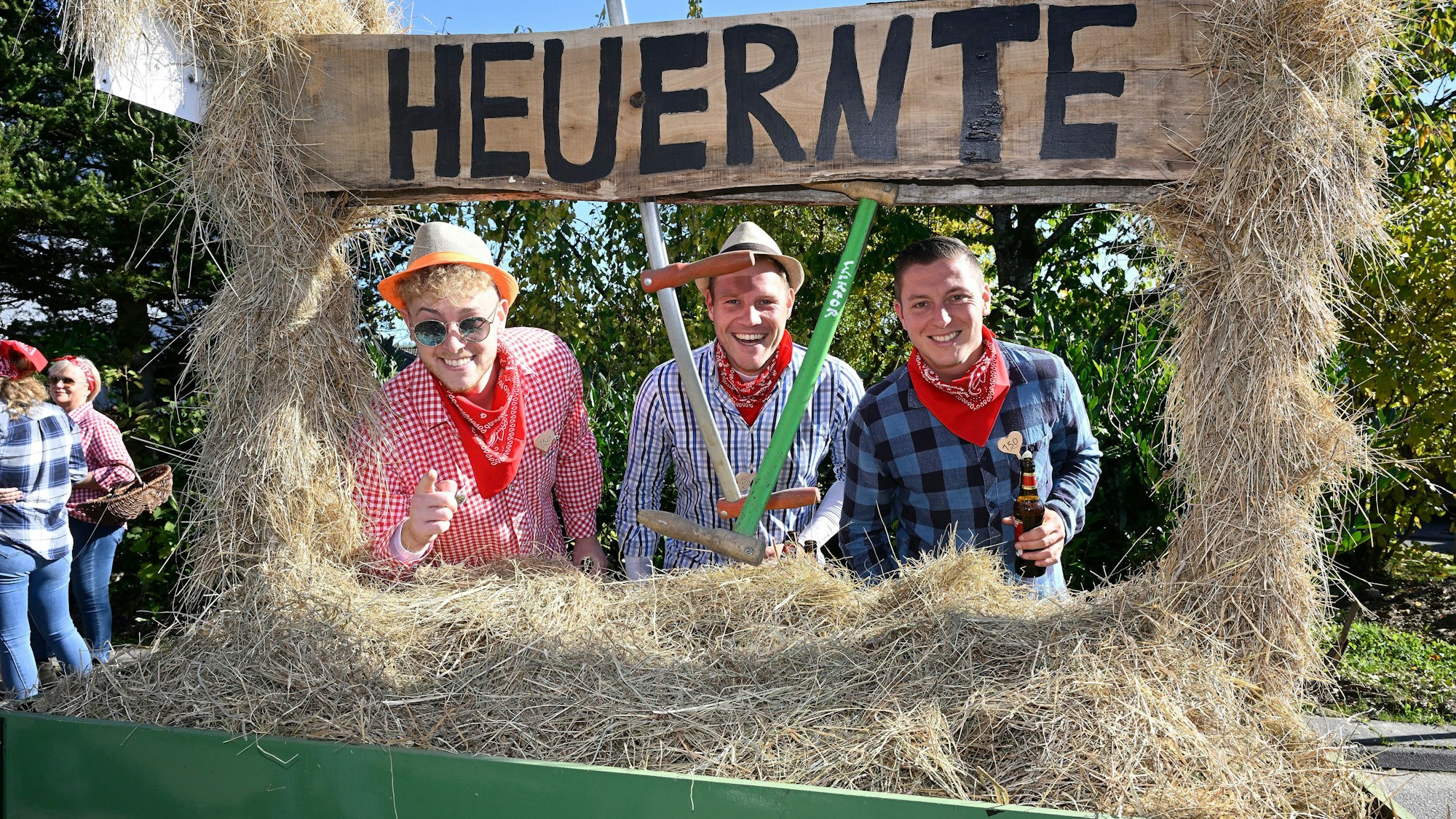 Drei Menschen stehen mit Arbeitsgerät hinter einem mit Heu beladenen Wagner.