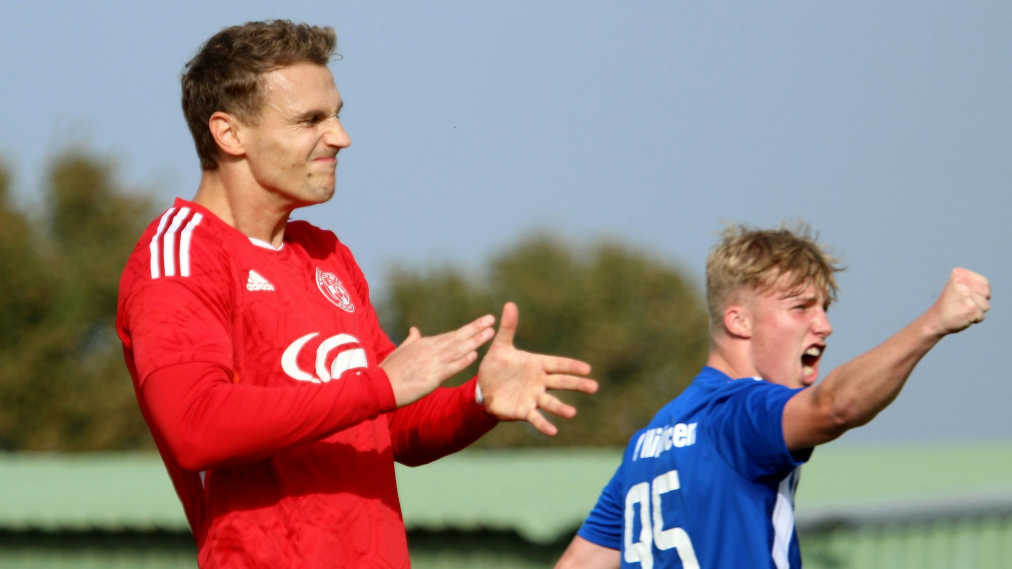 Ein Fußballspieler ärgert sich über seinen verschossenen Elfmeter. Ein Gegenspieler jubelt.