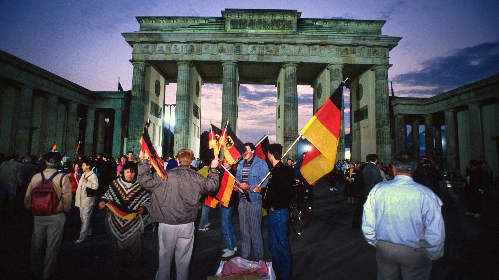 Menschen feiern mit Deutschland-Fahnen die deutsche Einheit vor dem Brandenburger Tor.