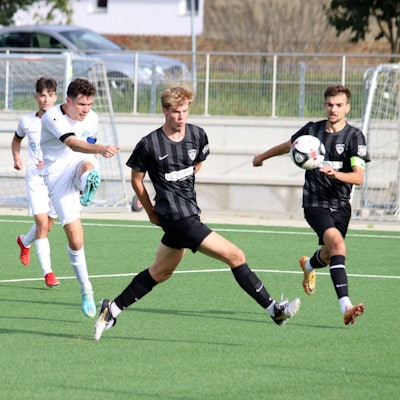Ein Fußballspieler schießt zwischen zwei Verteidigern hindurch. Einer von ihnen dreht dem Schützen den Rücken zu.