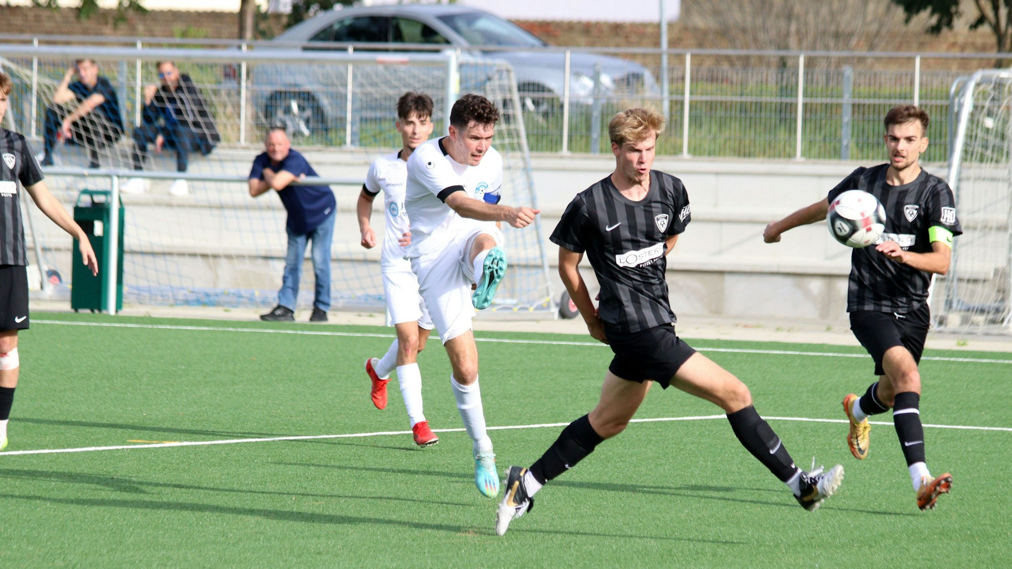 Ein Fußballspieler schießt zwischen zwei Verteidigern hindurch. Einer von ihnen dreht dem Schützen den Rücken zu.