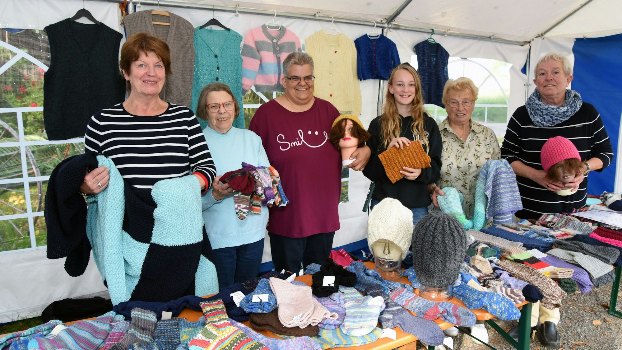 Sechs Frauen stehen an einem Stand, an dem sie selbstgestrickte Wollprodukte verkaufen.